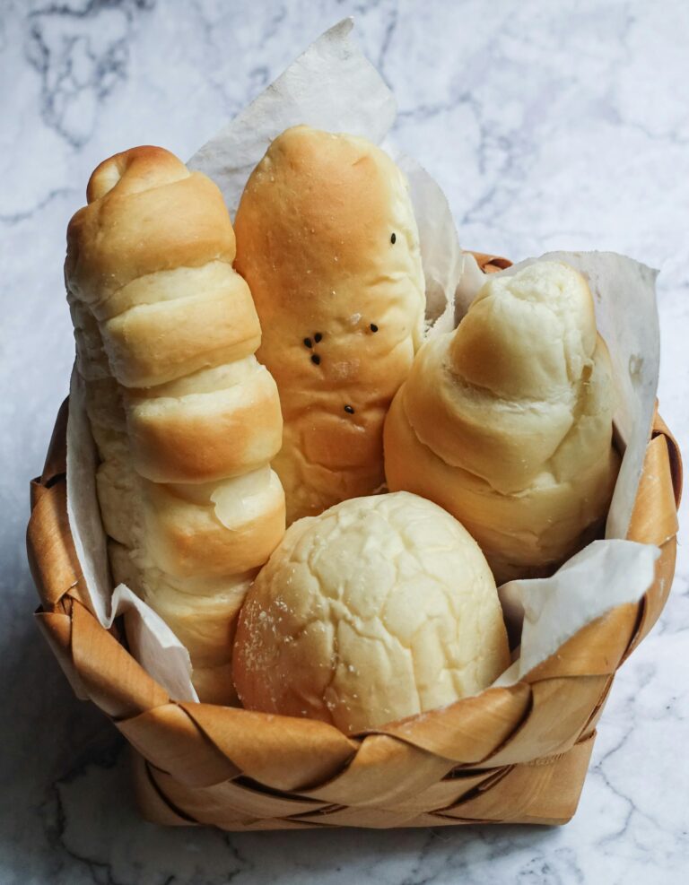 A variety of freshly baked breads in a wooden basket, displayed on a marble surface.