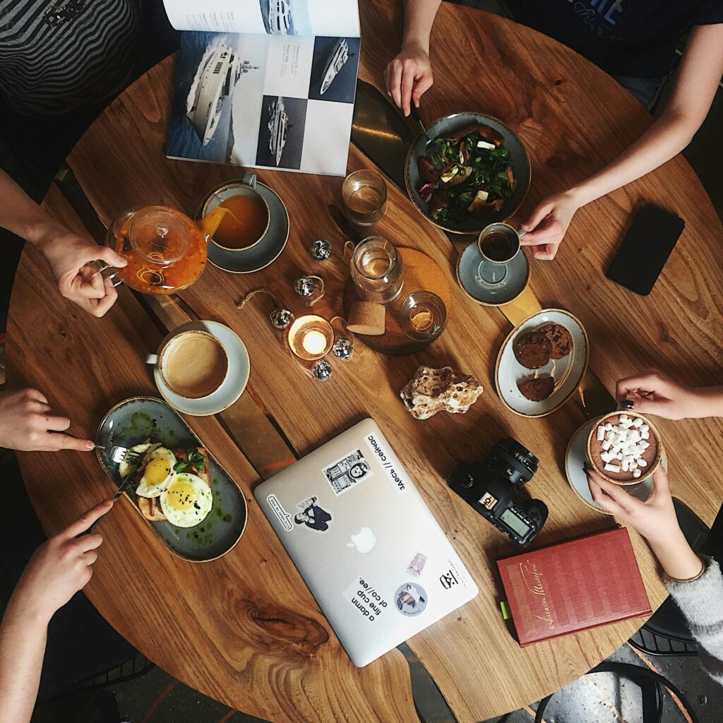 Overhead view of a cozy cafe setting with drinks, laptops, and books, perfect for teamwork or relaxation.