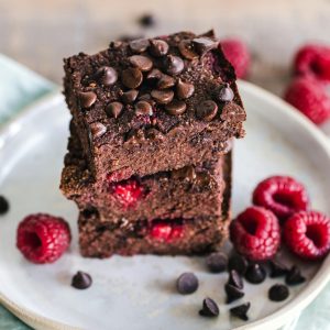 Close-up of deliciously indulgent chocolate raspberry brownies stacked on a ceramic plate with fresh raspberries.