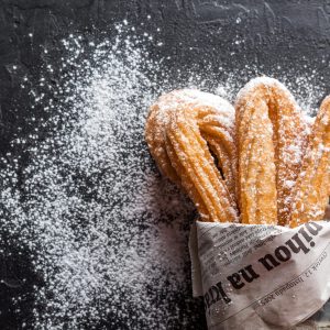 Close-up of freshly baked churros with powdered sugar on newspaper. A tasty dessert treat.